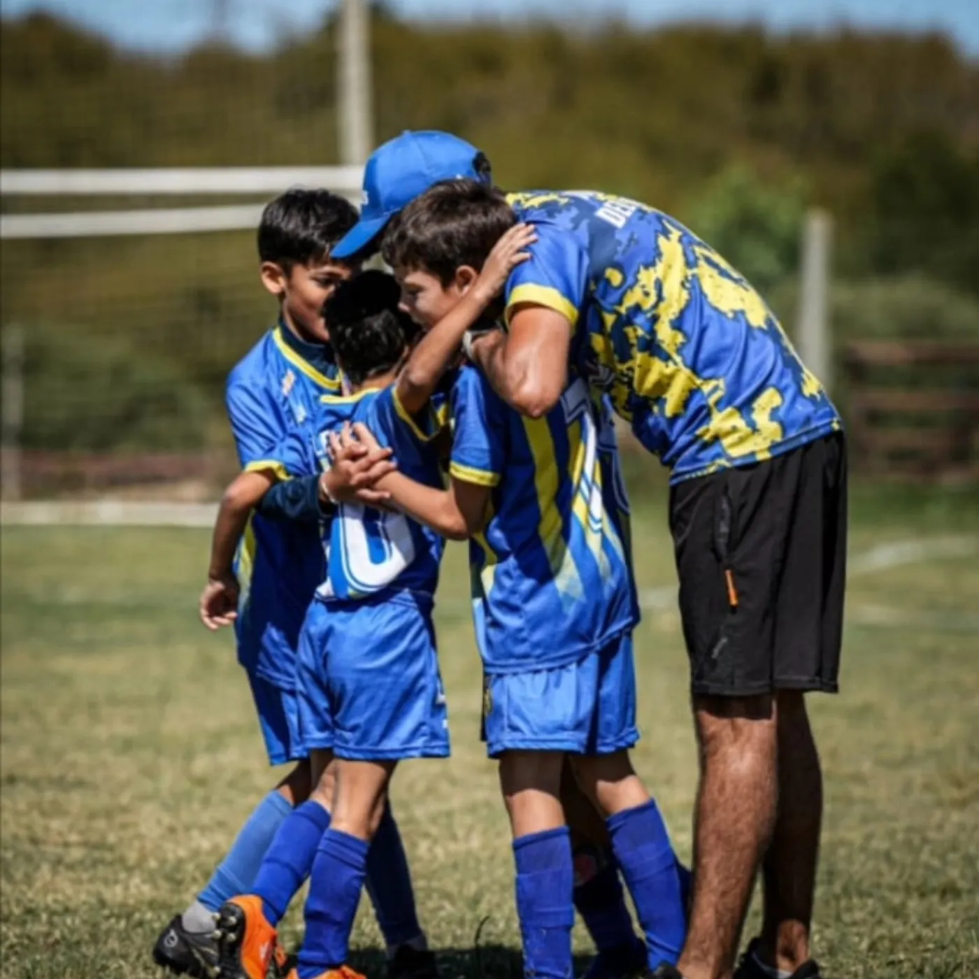 Un entrenador de Juveniles abrazado con varios jugadores en la cancha