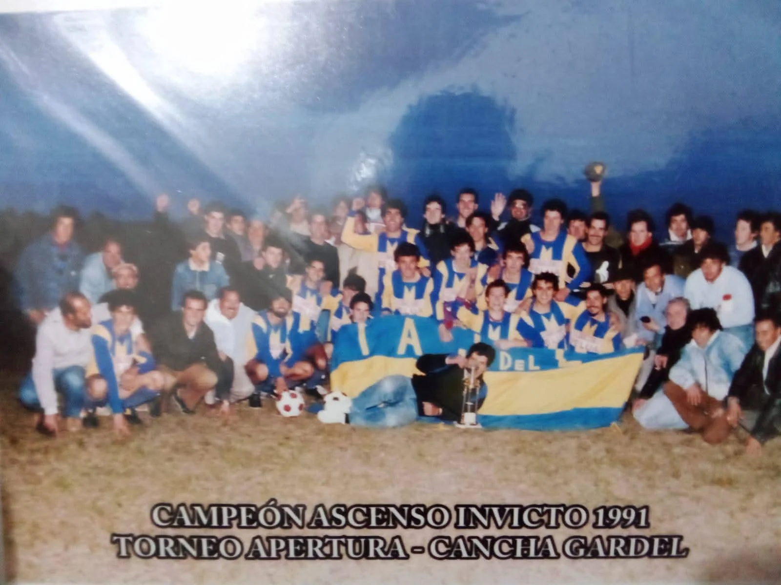 Celebración del título: Campeón Ascenso Invicto 1991, Torneo Apertura en Cancha Gardel, con la bandera del club y la copa.